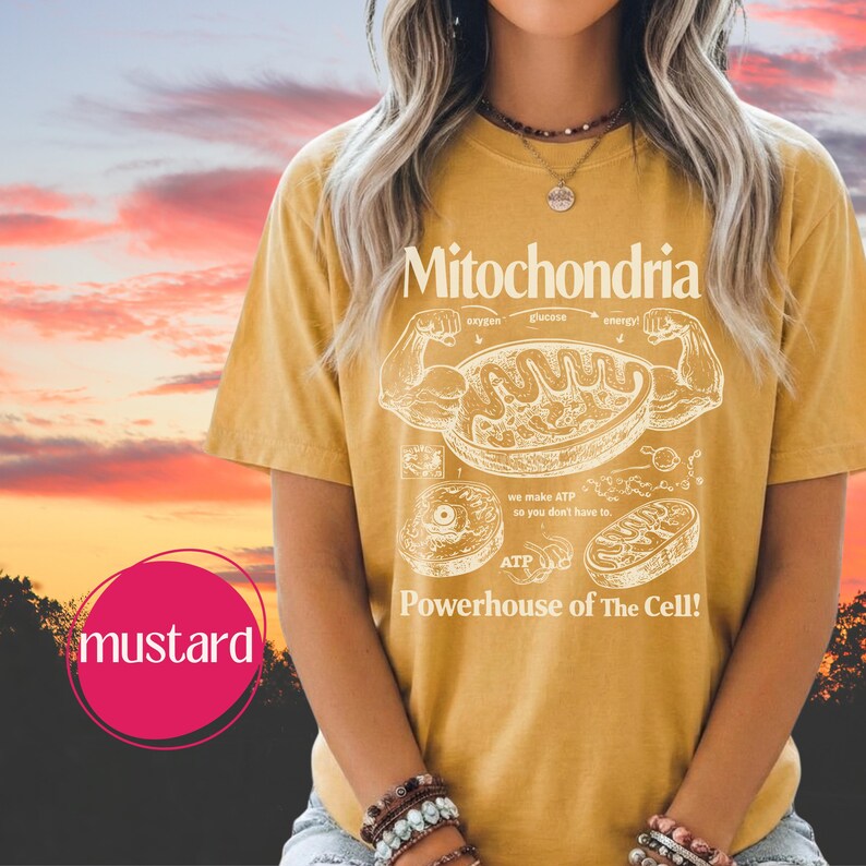 May include: Mustard-colored t-shirt with a white graphic of a cell's mitochondria and the text "Mitochondria Powerhouse of The Cell!". The shirt features a diagram of the cell's components and the words "oxygen", "glucose", and "energy".