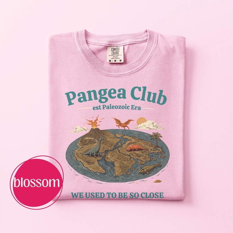 Peut inclure: T-shirt rose clair avec un motif graphique du Pangea Club. Le design pr&eacute;sente une carte du supercontinent avec des dinosaures, un volcan et le texte "WE USED TO BE SO CLOSE". Le t-shirt a un col rond et une &eacute;tiquette Comfort Colors.