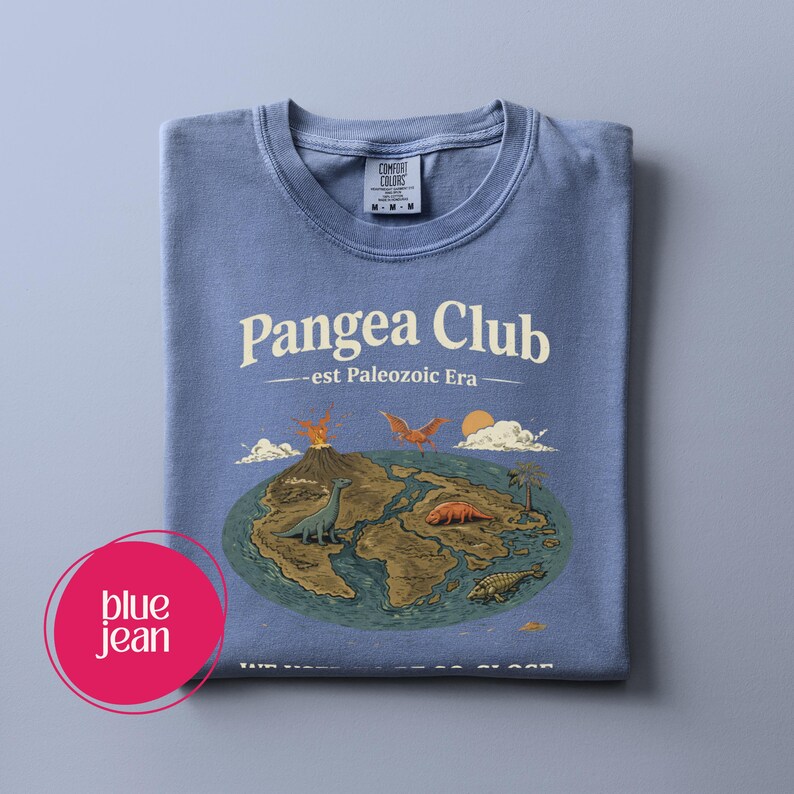 Peut inclure: T-shirt bleu jean pli&eacute; avec l'inscription "Pangea Club - est Paleozoic Era". Le motif repr&eacute;sente la Terre avec des dinosaures, des volcans et des palmiers. Le t-shirt porte une &eacute;tiquette Comfort Colors.