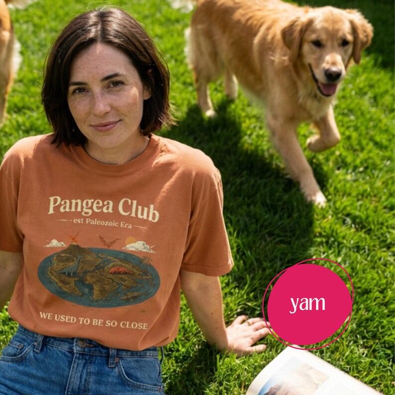 Peut inclure: Un t-shirt couleur rouille avec le texte "Pangea Club" et un graphique d'une carte et d'un volcan. Le t-shirt porte &eacute;galement le texte "est paleozoic Era" et "WE USED TO BE SO CLOSE". La personne porte un jean bleu et est assise sur de l'herbe verte.