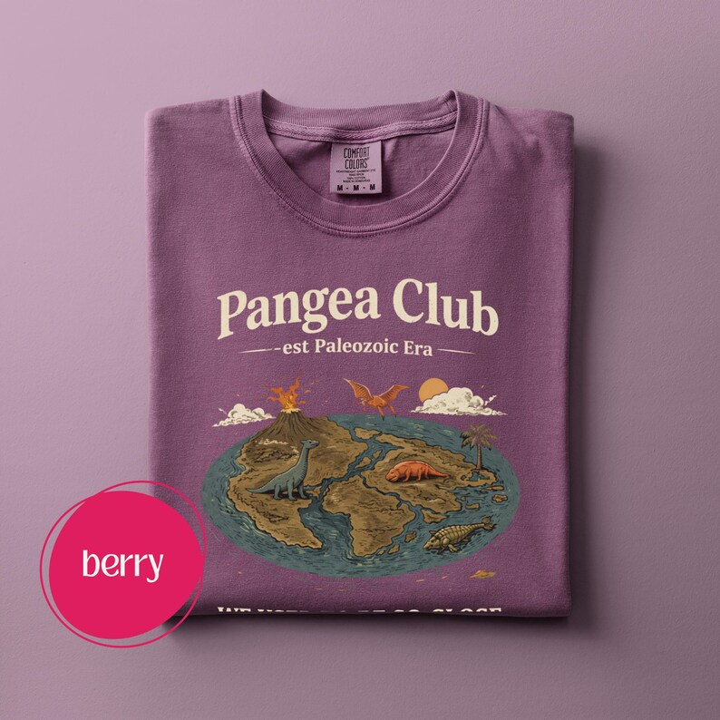 Peut inclure: Un t-shirt de couleur baie avec le texte "Pangea Club - est Paleozoic Era" et un graphisme de dinosaures sur une carte. Le t-shirt est pli&eacute; et porte une &eacute;tiquette "Comfort Colors".