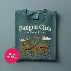 Peut inclure: T-shirt bleu &eacute;pic&eacute;a avec le texte "Pangea Club - est Paleozoic Era" et un dessin de dinosaures, d'un volcan et d'un soleil au-dessus d'une masse terrestre. Le t-shirt est pli&eacute; et porte une &eacute;tiquette Comfort Colors.