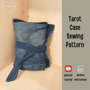 May include: A rolled-up denim tarot case tied with a matching fabric strap. The case is displayed in a wooden cabinet. Text on the right side reads "Tarot Case Sewing Pattern" with YouTube and written instructions icons.