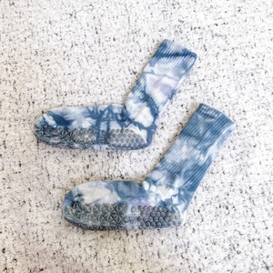 May include: A pair of tie-dye socks in shades of blue and white. The socks have a ribbed cuff and a non-slip grip sole. The tie-dye pattern is a mix of swirling and mottled designs. The socks are designed for comfort and style.