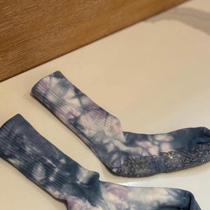 May include: A pair of tie-dye socks in shades of blue, purple, and white. The socks have a ribbed texture and a non-slip grip on the soles. The socks are designed for comfort and style.