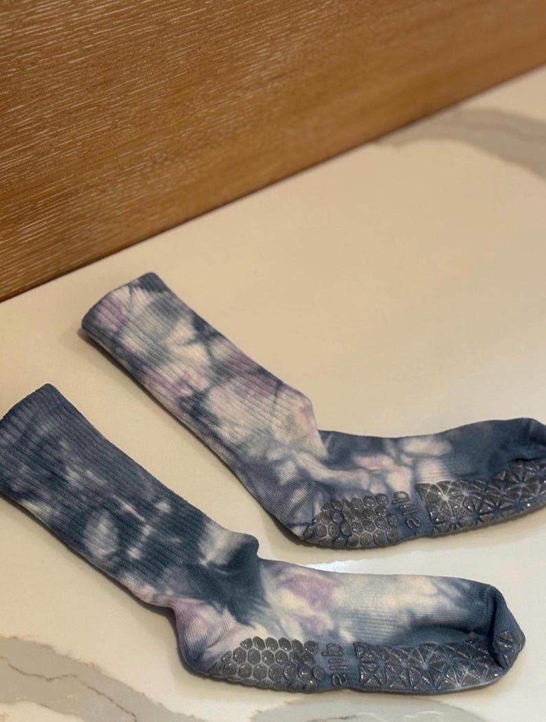 May include: A pair of tie-dye socks in shades of blue, purple, and white. The socks have a ribbed texture and a non-slip grip on the soles. The socks are designed for comfort and style.