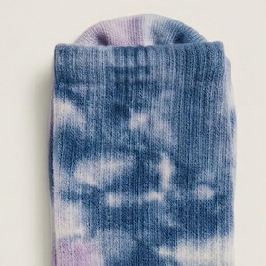 May include: Close-up of a tie-dye sock. The sock features a pattern of blue and white clouds against a blue background. The cuff of the sock is a light purple color.