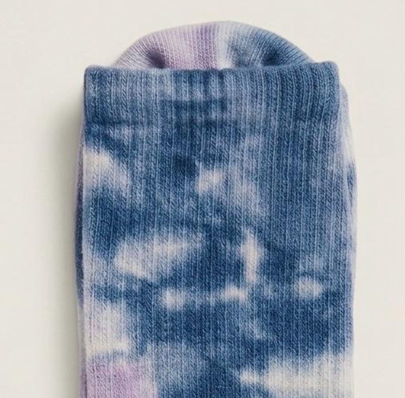 May include: Close-up of a tie-dye sock. The sock features a pattern of blue and white clouds against a blue background. The cuff of the sock is a light purple color.