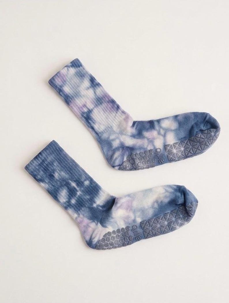 May include: A pair of tie-dye socks in shades of blue, purple, and white. The socks have a ribbed texture on the upper part and a non-slip grip on the soles. The socks are designed for comfort and style.