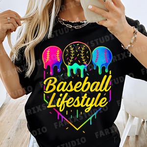 May include: Black t-shirt with a colorful graphic design. The design features three baseballs with dripping paint effects in pink, yellow, and blue. The text "Baseball Lifestyle" is in a yellow, stylized font.