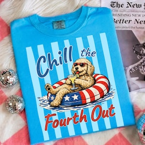May include: A bright blue t-shirt featuring a graphic of a golden-colored dog wearing red sunglasses, relaxing in a red, white, and blue striped pool float while holding a cocktail. The text reads Chill the Fourth Out in blue and red letters.