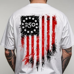 以下が含まれることがあります： 背面にぼろぼろのアメリカ国旗のデザインが施された白いTシャツ。旗は黒と赤の配色で、左上に数字の「250」があります。デザインには星とストライプが含まれています。