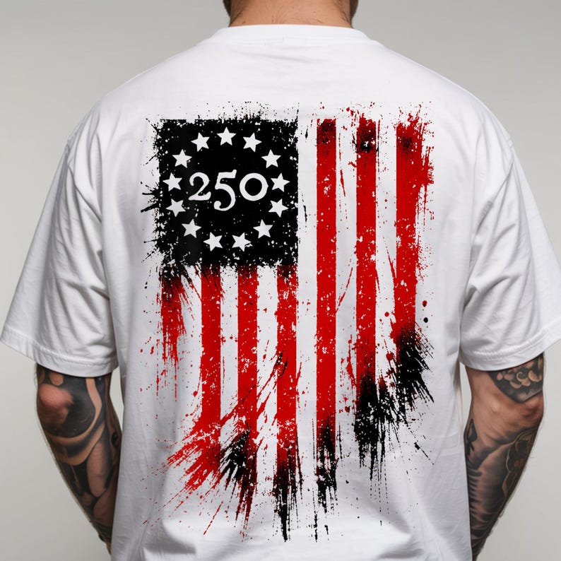 以下が含まれることがあります： 背面にぼろぼろのアメリカ国旗のデザインが施された白いTシャツ。旗は黒と赤の配色で、左上に数字の「250」があります。デザインには星とストライプが含まれています。