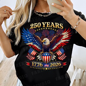 May include: Black t-shirt featuring a patriotic design with an eagle, American flags, and fireworks. The shirt displays the text "250 YEARS", "1776", and "2026", celebrating a historical milestone. The eagle's wings are colored in the American flag's colors.