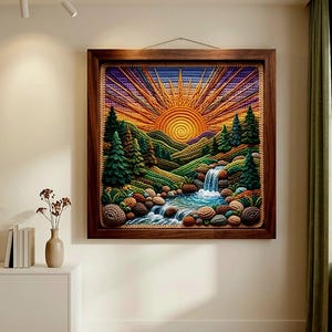 May include: A framed, textured artwork depicting a sunset over a mountain landscape. The piece features a waterfall, river, and trees, with a color palette of orange, green, and blue. The frame is a dark brown wood.