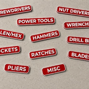 Może przedstawiać: Kolekcja prostokątnych czerwonych tabliczek z białymi obwódkami i białym tekstem. Tabliczki mają napisy: SCREWDRIVERS, NUT DRIVERS, POWER TOOLS, WRENCHES, ALLEN/HEX, HAMMERS, DRILL BITS, SOCKETS, RATCHES, BLADES, PLIERS oraz MISC.