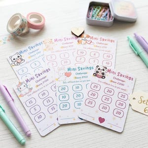May include: A set of six Mini Savings Challenge cards featuring cartoon animals, numbered boxes for tracking savings, and the text Mini Savings Challenge. The set includes pastel pens, washi tape, and a small tin of paper clips for organisation.