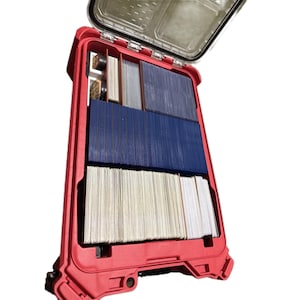 May include: A bright red hard-shell storage case with an open lid, containing multiple organised rows of trading cards. The interior features custom dividers separating stacks of cards in white, blue, and grey sleeves, along with small circular tokens.
