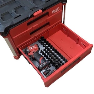 May include: A red and black Milwaukee PACKOUT tool storage unit with an open drawer containing a red and black cordless impact driver, a battery pack, and an organised foam insert holding numerous black metal socket attachments.