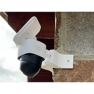 Könnte beinhalten: Eine weiße Eufy Security Kamera mit schwarzem, kugelförmigem Objektivgehäuse, die an einer Steinmauer montiert ist. Das Gerät verfügt über ein weißes Solarpanel an der Oberseite, eine mit Schrauben befestigte weiße Halterung und das Eufy Security Logo.