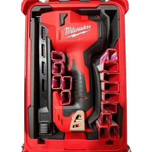 Op de afbeelding: Een rood-zwarte Milwaukee accunagelpistool in een op maat gemaakte rode kunststof koffer. Het gereedschap wordt vergezeld door verschillende rijen metalen nagels in het gevormde schuiminterieur, voorzien van het Milwaukee merklogo.