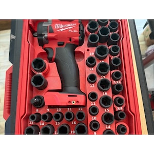 May include: A red and black Milwaukee Fuel cordless impact wrench stored in a red moulded plastic case alongside a comprehensive set of black impact sockets, each clearly labelled with its specific size in inches and metric measurements.