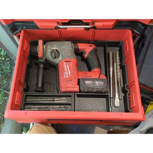 Könnte beinhalten: Ein rot-schwarzer Milwaukee M18 Akku-Bohrhammer in einem roten Kunststoff-Werkzeugkasten-Organizer. Das Set enthält einen Akku, einen Seitengriff sowie mehrere Metallbohrer und Meißel, die in geformten Fächern angeordnet sind.