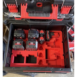 Peut inclure: Coffre à outils noir et rouge avec un intérieur rouge. L'intérieur contient plusieurs batteries M18 6.0 Ah noires et rouges, et d'autres accessoires d'outils électriques rouges. La boîte à outils est ouverte, révélant le contenu.