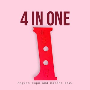 May include: A red, angled tool with the text "4 IN ONE" at the top and "Angled cups and matcha bowl" at the bottom. The tool has two circular holes and a unique shape, set against a light pink background.