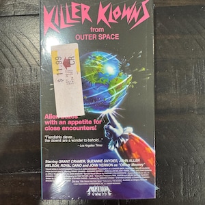 May include: A VHS tape of the movie "Killer Klowns from Outer Space." The cover features the title in pink, a clown's hand pointing at a globe, and the tagline "Aliens with an appetite for close encounters!"