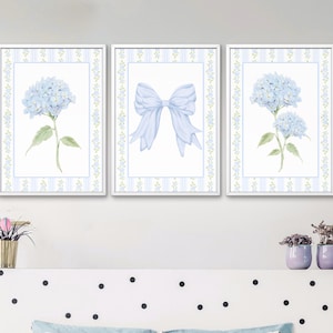 May include: Three framed watercolor prints featuring a light blue hydrangea flower, a light blue bow, and another hydrangea. Each print has a white border with a light blue and green floral pattern. The prints are displayed above a bed with a polka dot headboard.