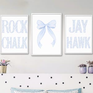 Op de afbeelding: Drie ingelijste wandkunstprints. Eén print zegt "ROCK CHALK" in lichtblauwe letters met een bloemenpatroon. Een andere print toont een lichtblauwe strik. De derde print zegt "JAY HAWK" in lichtblauwe bloemenletters.