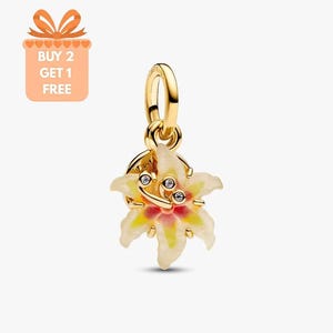 Könnte beinhalten: Ein goldfarbener Charm mit einem Blumendesign. Die Blume hat weiße, gelbe und rosa Blütenblätter mit drei kleinen, klaren Steinen in der Mitte. Der Charm hat oben eine Schlaufe zum Befestigen an einem Armband oder einer Halskette.