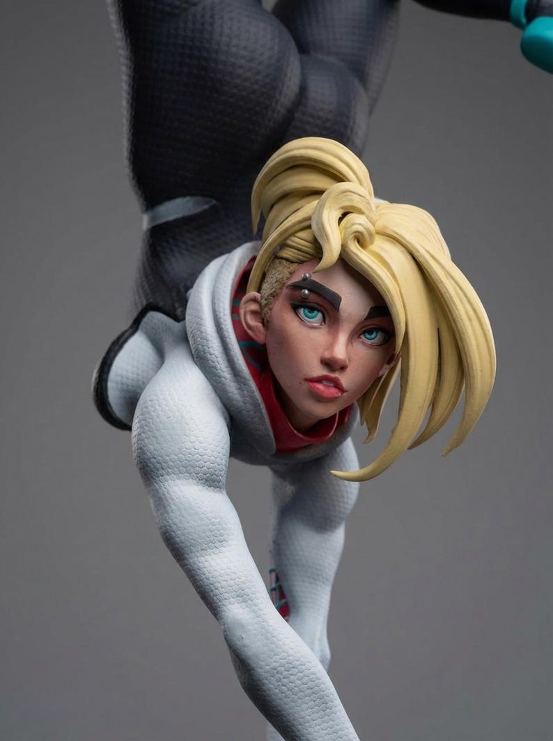 May include: A detailed figurine of a character with blonde hair styled in a high ponytail and a white hoodie with red accents. The figure is in a dynamic pose, with a black textured suit visible.