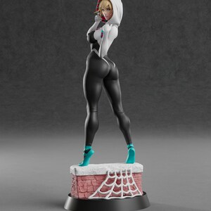 May include: A figurine of a female superhero in a black and white suit with a hood. The figure is standing on a brick chimney with a white spiderweb design. The figure is wearing teal shoes.