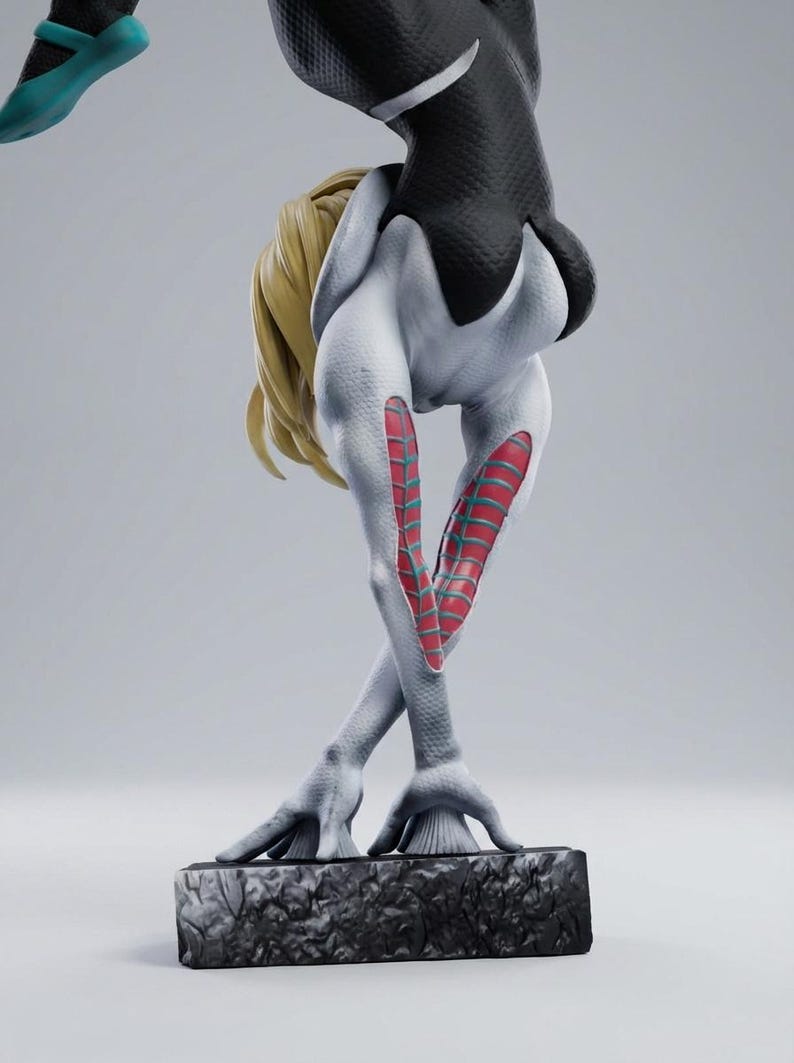May include: A detailed figurine of a superheroine in a dynamic pose. The figure is predominantly white with black accents and red and teal details. The blonde hair contrasts with the dark suit. The figure is on a textured base.