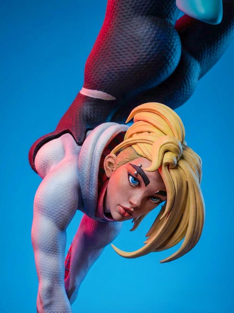 May include: A detailed figurine of a female character with blonde hair and blue eyes, wearing a white and black bodysuit. The figure is posed against a blue backdrop, showcasing intricate details and dynamic form.