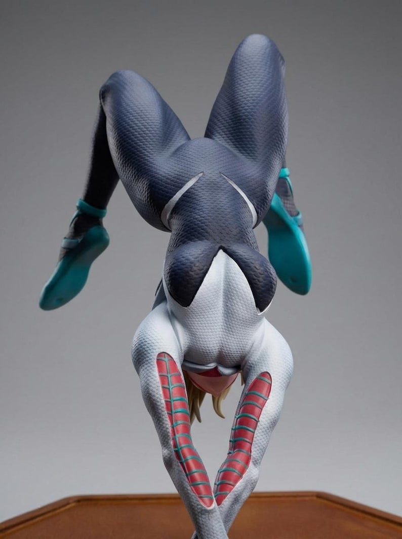 May include: A figurine of a character in a dynamic pose, wearing a white and navy blue suit with teal accents. The figure is upside down, showcasing the intricate design and textures of the costume.