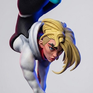 May include: A detailed figurine of a female superhero in a dynamic pose. She wears a white and black suit with a hood, and her blonde hair is styled in a unique fashion. The figure has blue eyes and a determined expression.