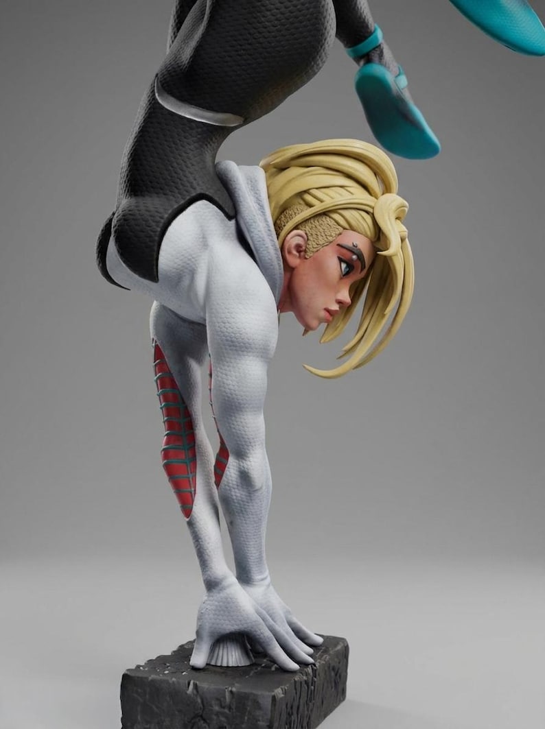 May include: A detailed figurine of a character in a dynamic pose, wearing a white and black suit with red accents. The figure has blonde hair and is positioned in a handstand, showcasing athletic form. The base is a textured, dark gray block.