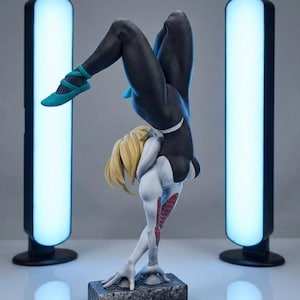 May include: A detailed figurine of a character in a black and white suit, with blonde hair, striking a handstand pose. The figure is on a textured base, with teal shoes. Two tall, glowing blue lights flank the figure.
