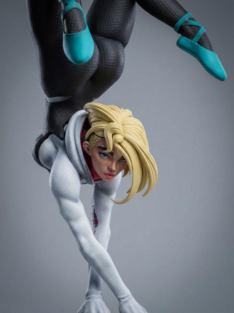 May include: A detailed figurine of a female character in a dynamic pose. She wears a white hoodie, a black bodysuit, and teal ballet flats. Her blonde hair is styled, and she has blue eyes. The figure is set against a gray backdrop.