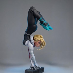 May include: A detailed figurine of a character in a dynamic handstand pose. The figure wears a black and white suit with blue accents and shoes. The character has blonde hair and is balanced on a black rectangular base.