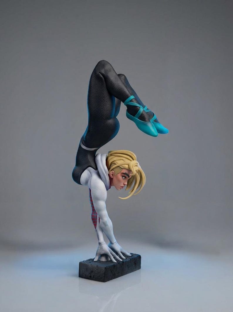 May include: A detailed figurine of a character in a dynamic handstand pose. The figure wears a black and white suit with blue accents and shoes. The character has blonde hair and is balanced on a black rectangular base.