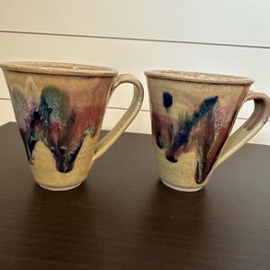 Könnte beinhalten: Eine weiße Keramik-Tasse mit schwarzem Henkel und dem Text "But First, Coffee" in fetter, schwarzer Schrift. Die Tasse steht vor einem neutralen Hintergrund, der ihr schlichtes Design hervorhebt.