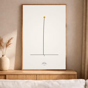 May include: A framed art print with a minimalist design. A thin black line rises from a horizontal line, topped with a small yellow circle. The text "The Toss" is printed at the bottom of the print.
