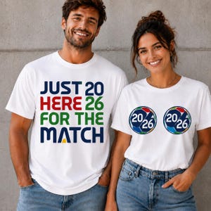 Puede incluir: Dos camisetas blancas. Una tiene el texto "JUST 20 HERE 26 FOR THE MATCH" en azul, rojo, verde y amarillo. La otra tiene dos gr&aacute;ficos de bal&oacute;n de f&uacute;tbol con "20/26" en su interior.