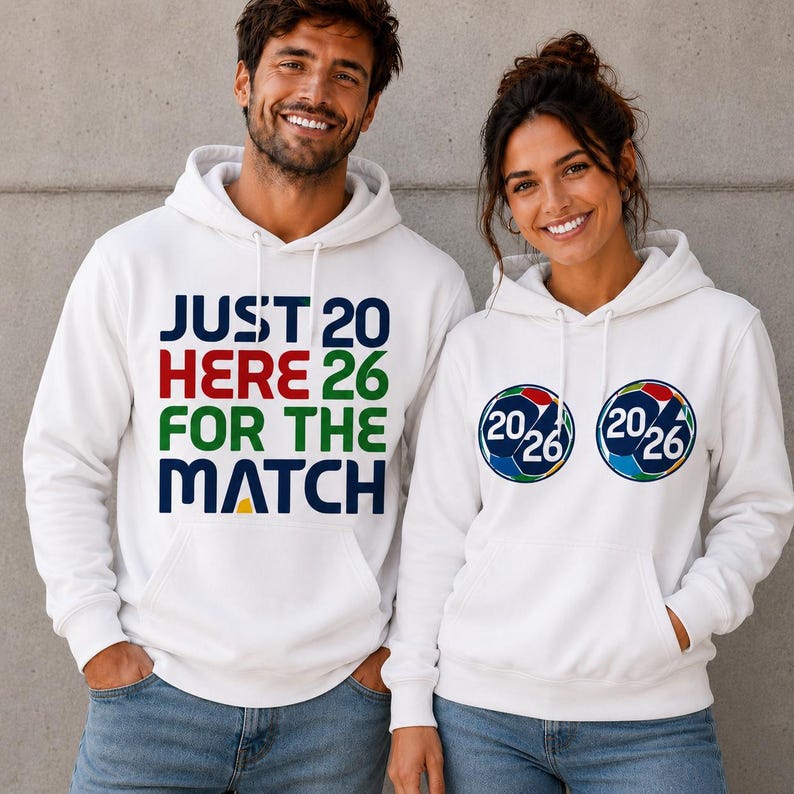 Puede incluir: Sudaderas con capucha blancas. Una tiene el texto "JUST 20 HERE 26 FOR THE MATCH" en azul, rojo, verde y amarillo. La otra tiene dos gr&aacute;ficos de bal&oacute;n de f&uacute;tbol con "20/26". Ambos llevan vaqueros azules.