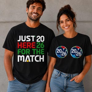 Puede incluir: Dos personas con camisetas negras. Una camiseta tiene el texto "JUST HERE FOR THE MATCH" en blanco, rojo y verde. La otra camiseta tiene dos gr&aacute;ficos de bal&oacute;n de f&uacute;tbol con "20/26" en su interior. Ambas camisetas son negras.