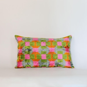 May include: Rectangular decorative pillow with a geometric pattern. The pillow features a gray background with a repeating pattern of pink, orange, and green squares. The pillow has a soft, velvety texture.